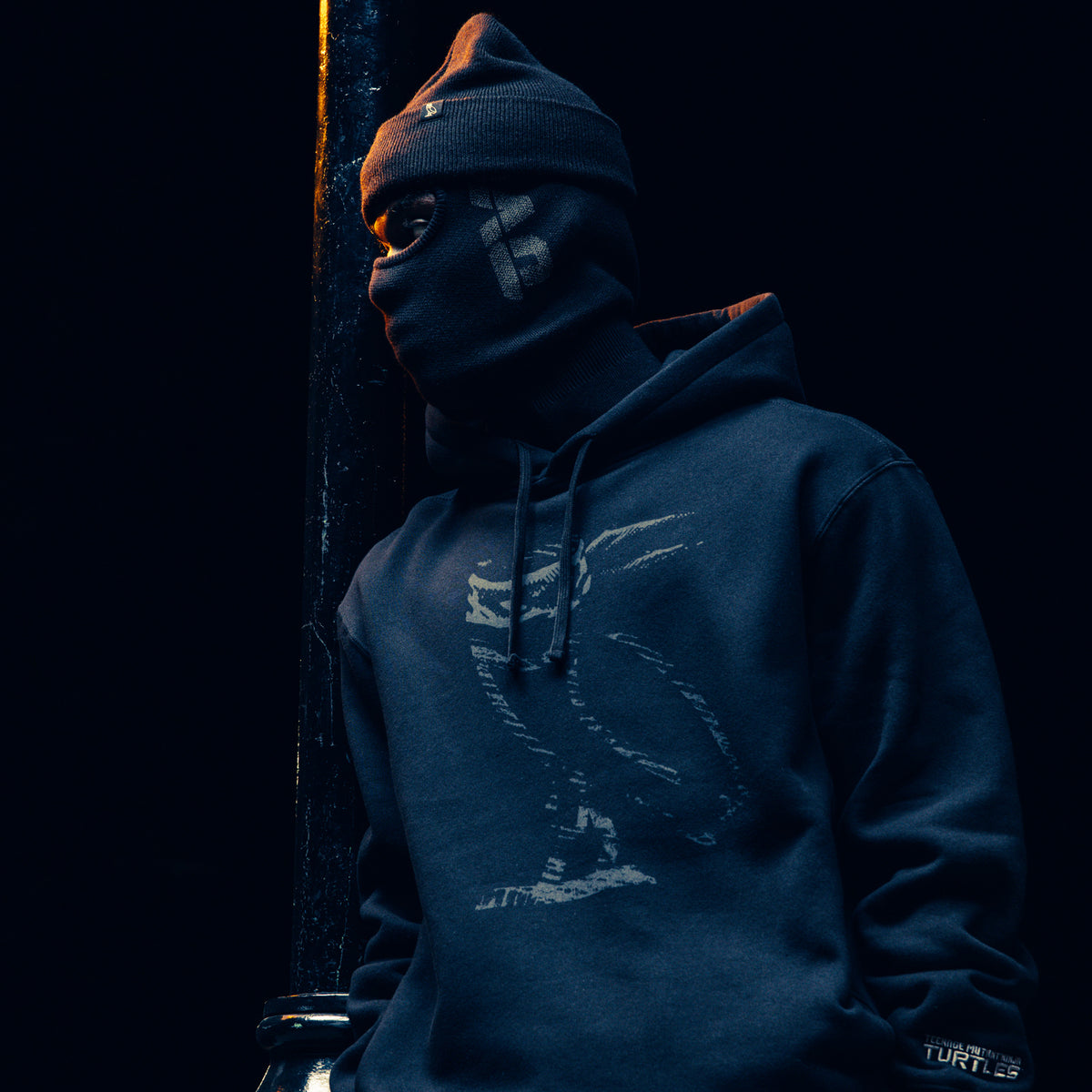 Person wearing a dark October's Very Own hoodie and beanie in a dimly lit setting