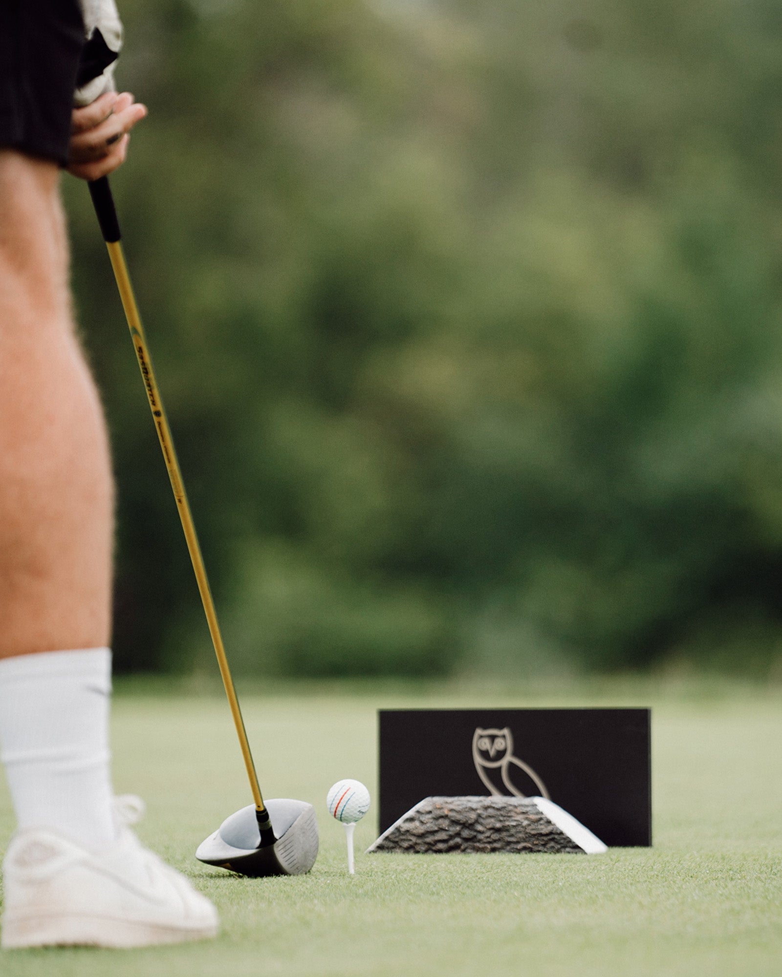 Golfer preparing to hit a golf ball with a putter on a green with October's Very Own logo in the background