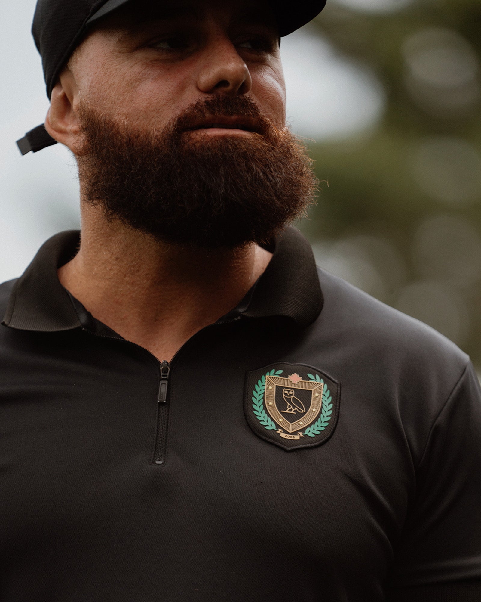 Man wearing a black jacket with a October's Very Own logo on a blurred natural background