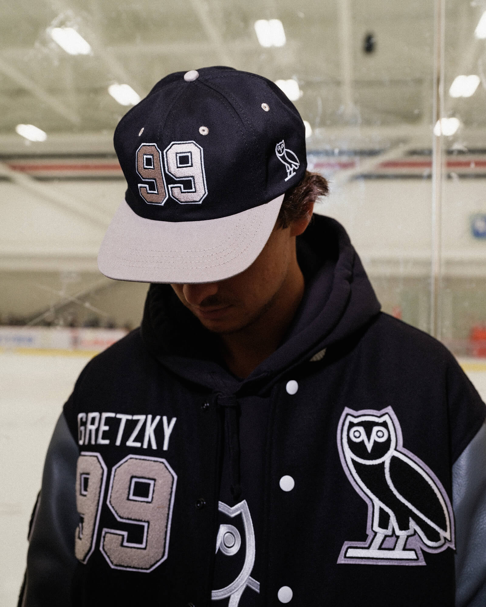 Person wearing a black and white cap with number 99 and a black jacket with 'Gretzky' and number 99, indoors.