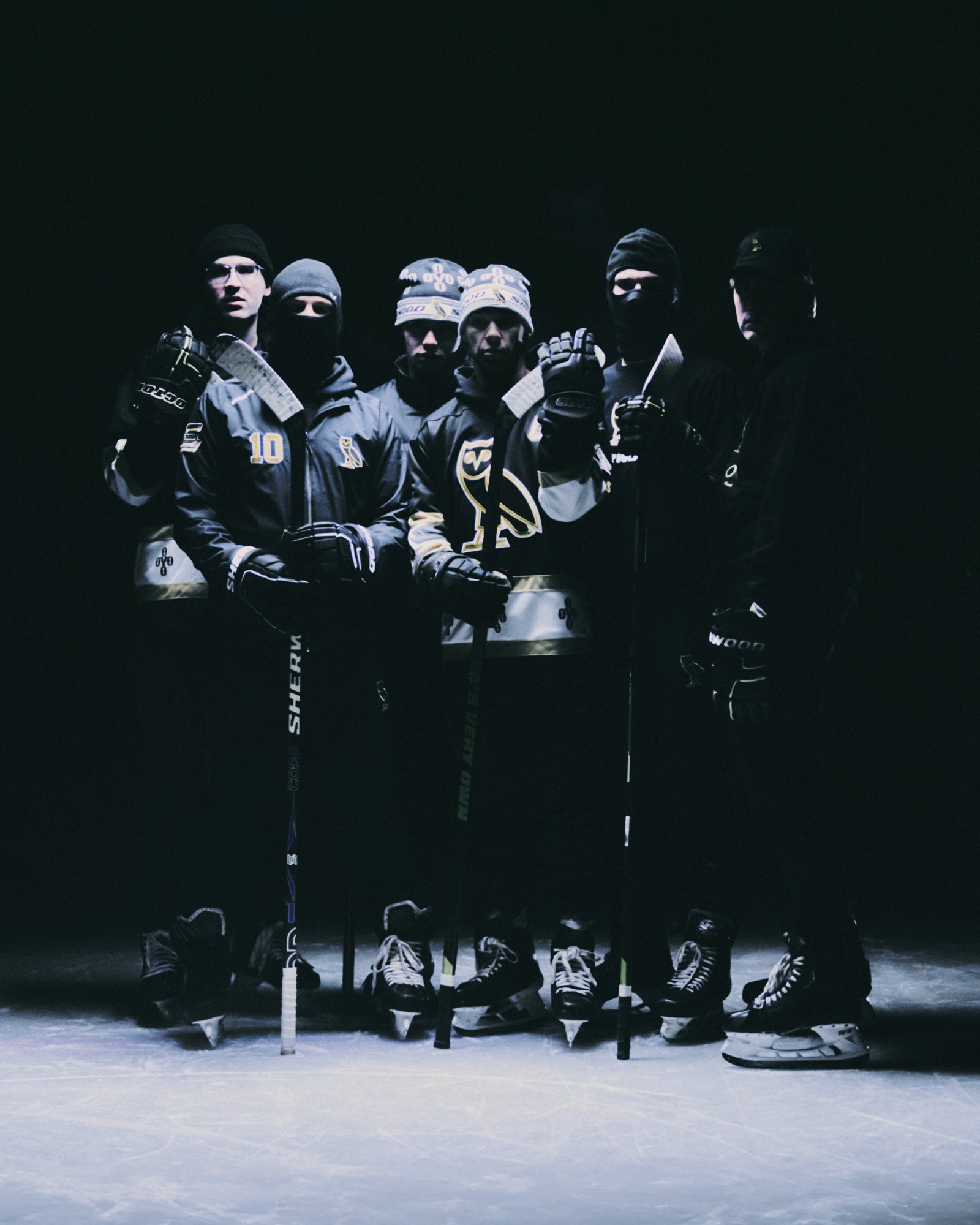 Group of hockey players in black October's Very Own hockey jerseys with masks on a dark ice rink.