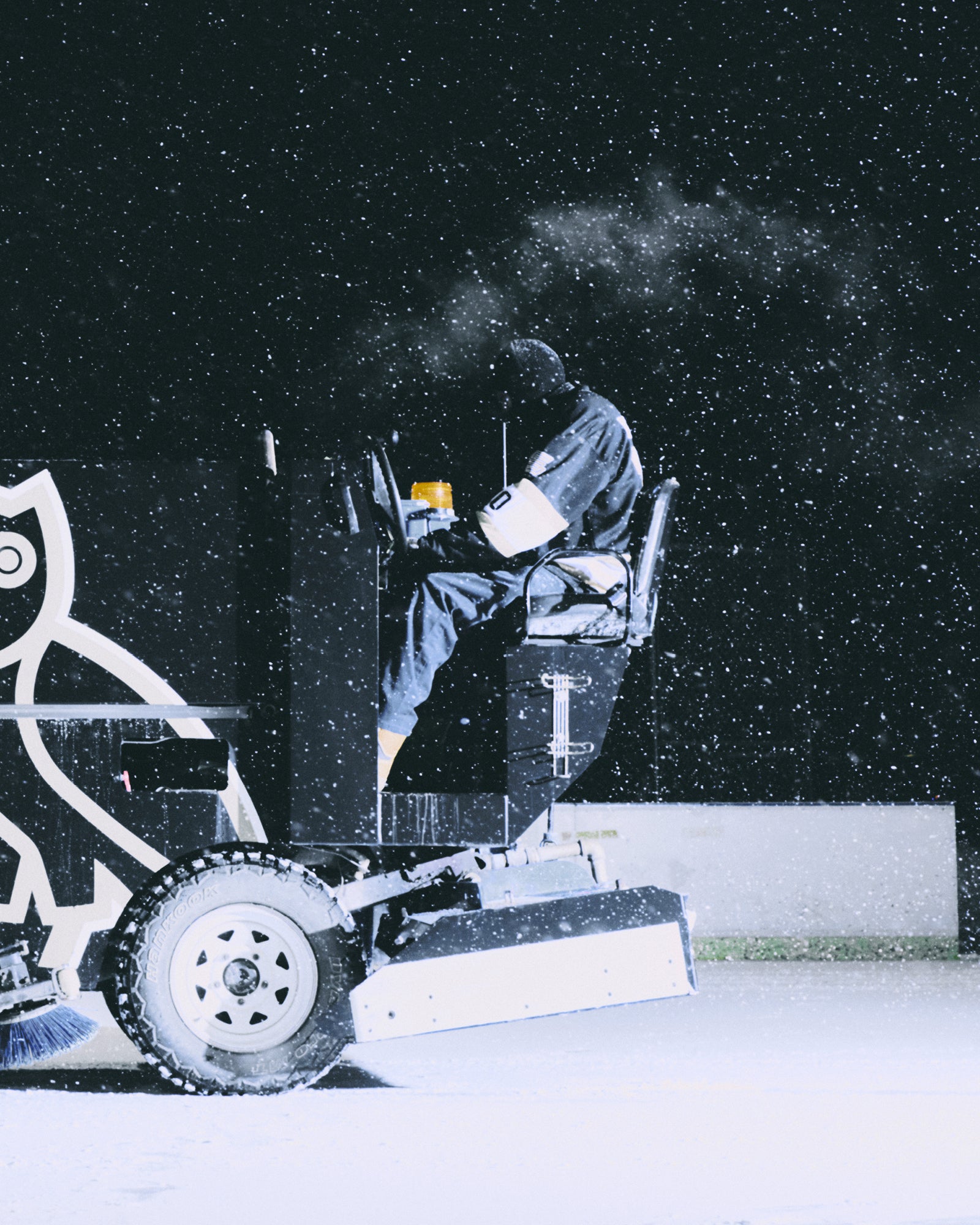 Person using a Zamboni in a snowy outdoor setting
