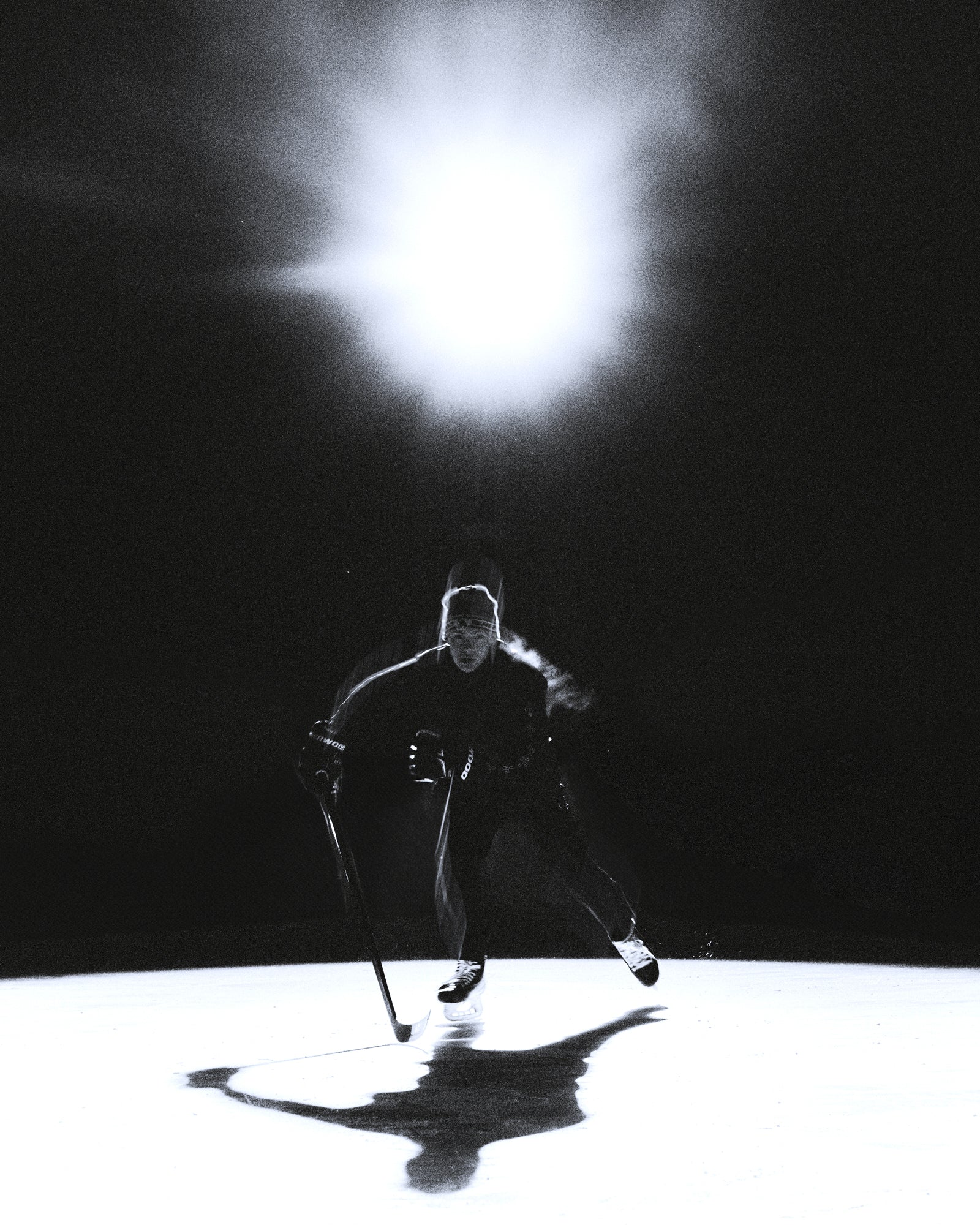 Person playing hockey on a dark ice rink with a bright light source in the background