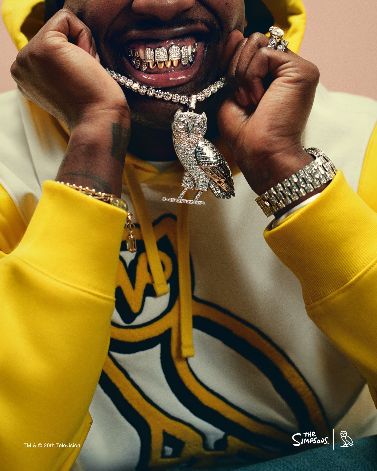 Lil Yachty wearing a October's Very Own yellow hoodie with a prominent owl pendant and jewelry, against a pink background.