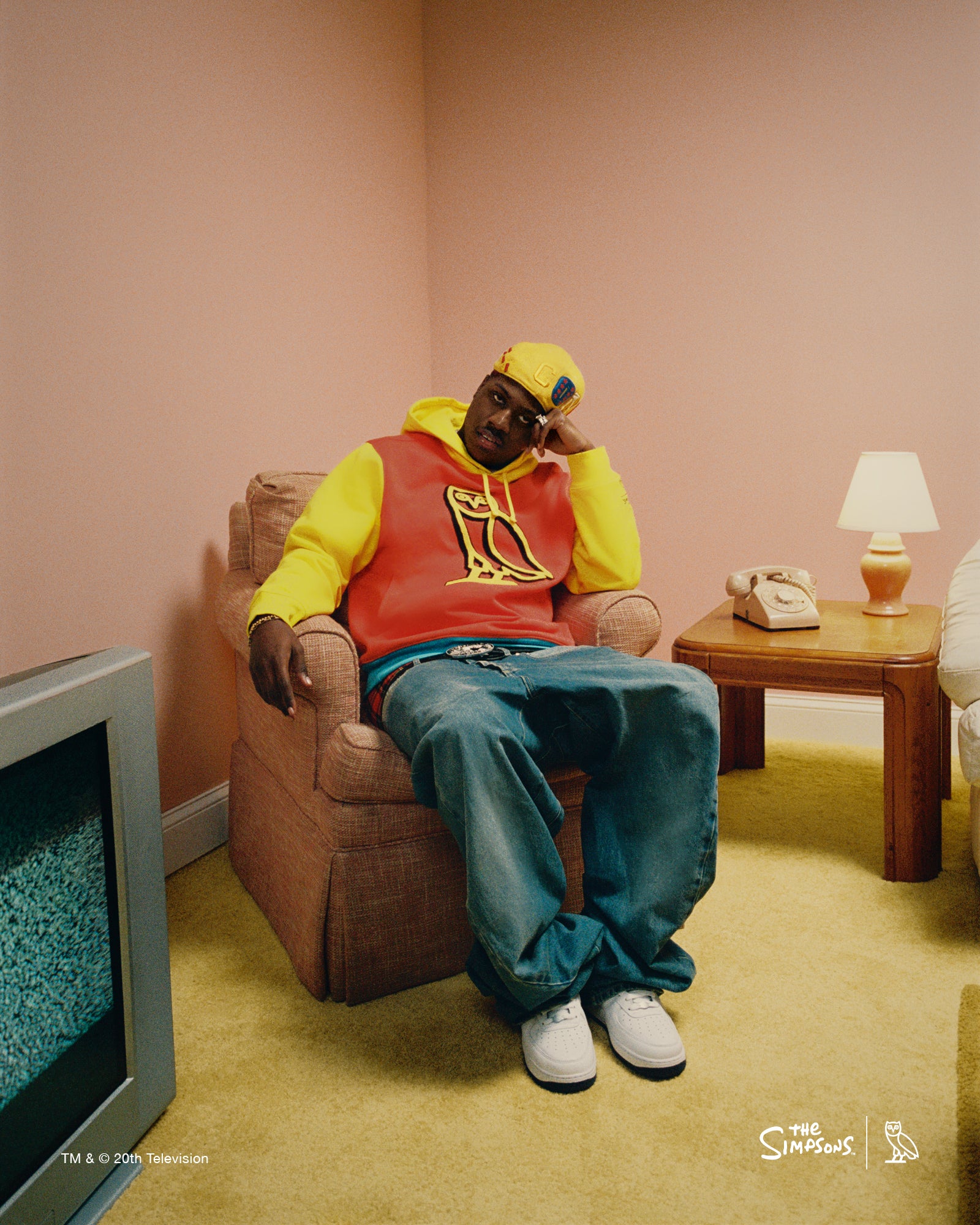Lil Yachty wearing a October's Very Own colorful outfit sitting in a room with a television and lamp.