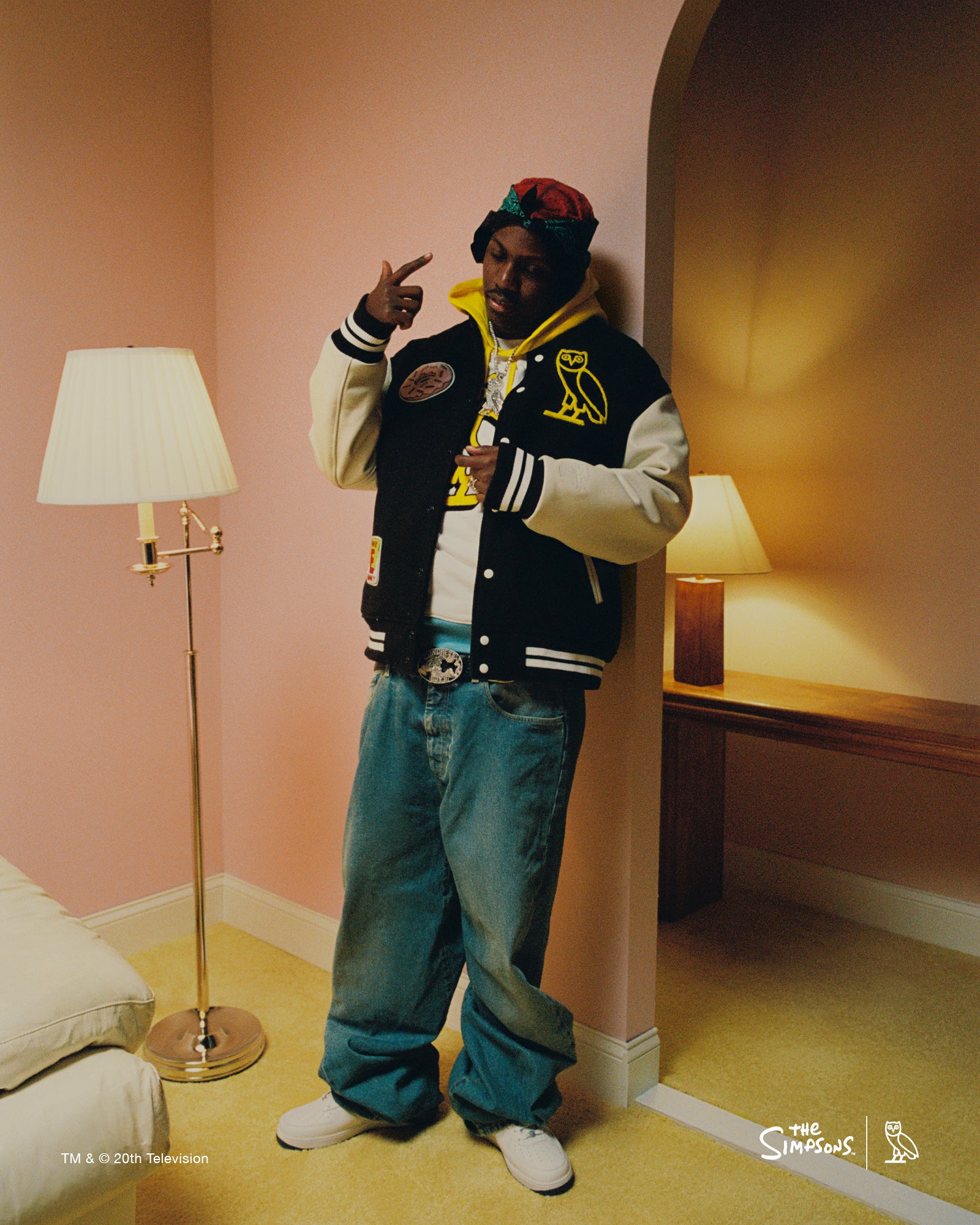 Lil Yachty wearing a October's Very Own varsity jacket and blue pants in a room with pink walls and lamps.