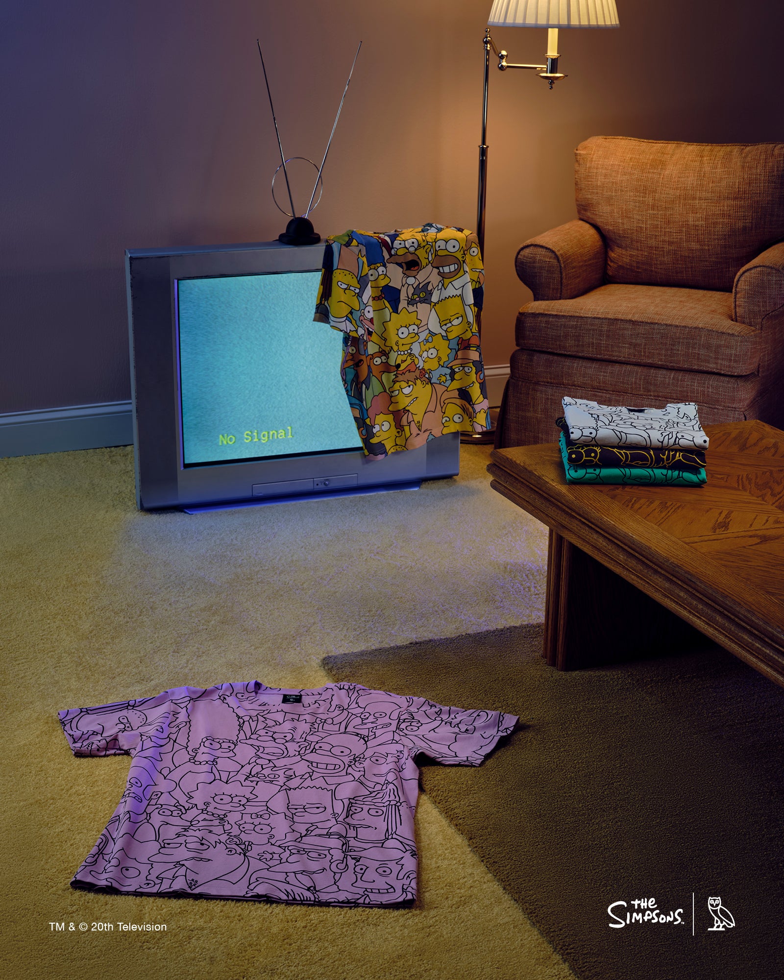 Living room with a television and October's Very Own x The Simpsons t-shirt, surrounded by patterned shirts on a carpeted floor.