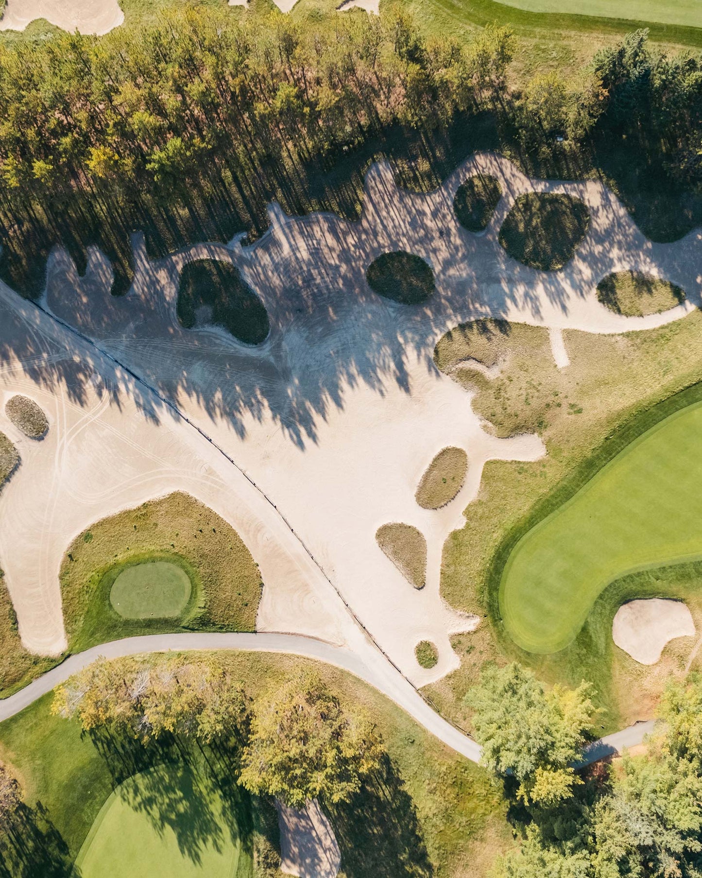 Aerial view of a golf course with sand bunkers, tree-lined fairways, and manicured greens.