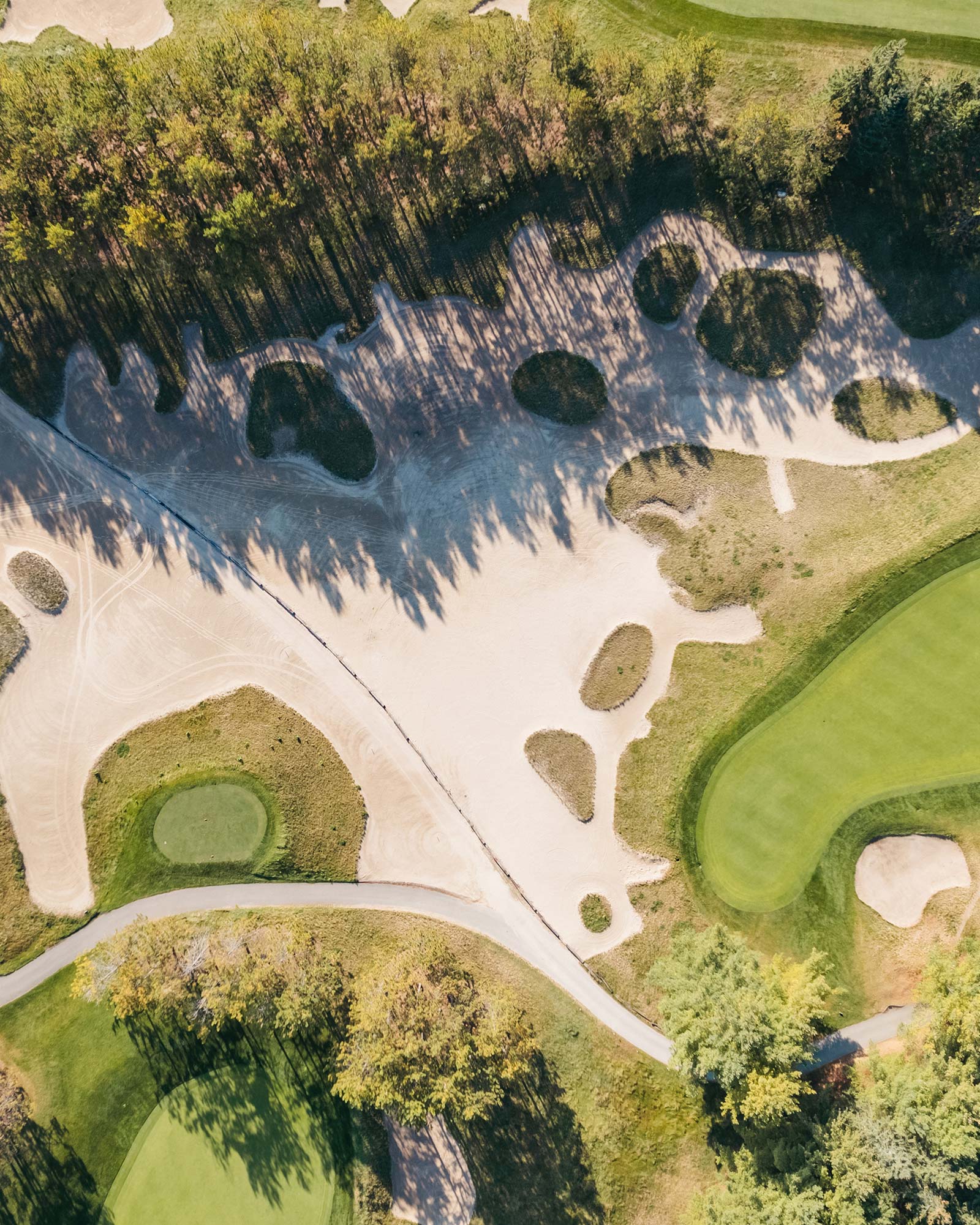 Aerial view of a golf course with sand bunkers, tree-lined fairways, and manicured greens.