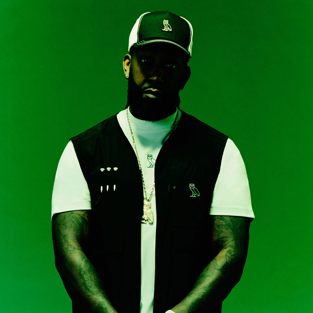 Person wearing a October's Very Own black vest over a white shirt with a green background
