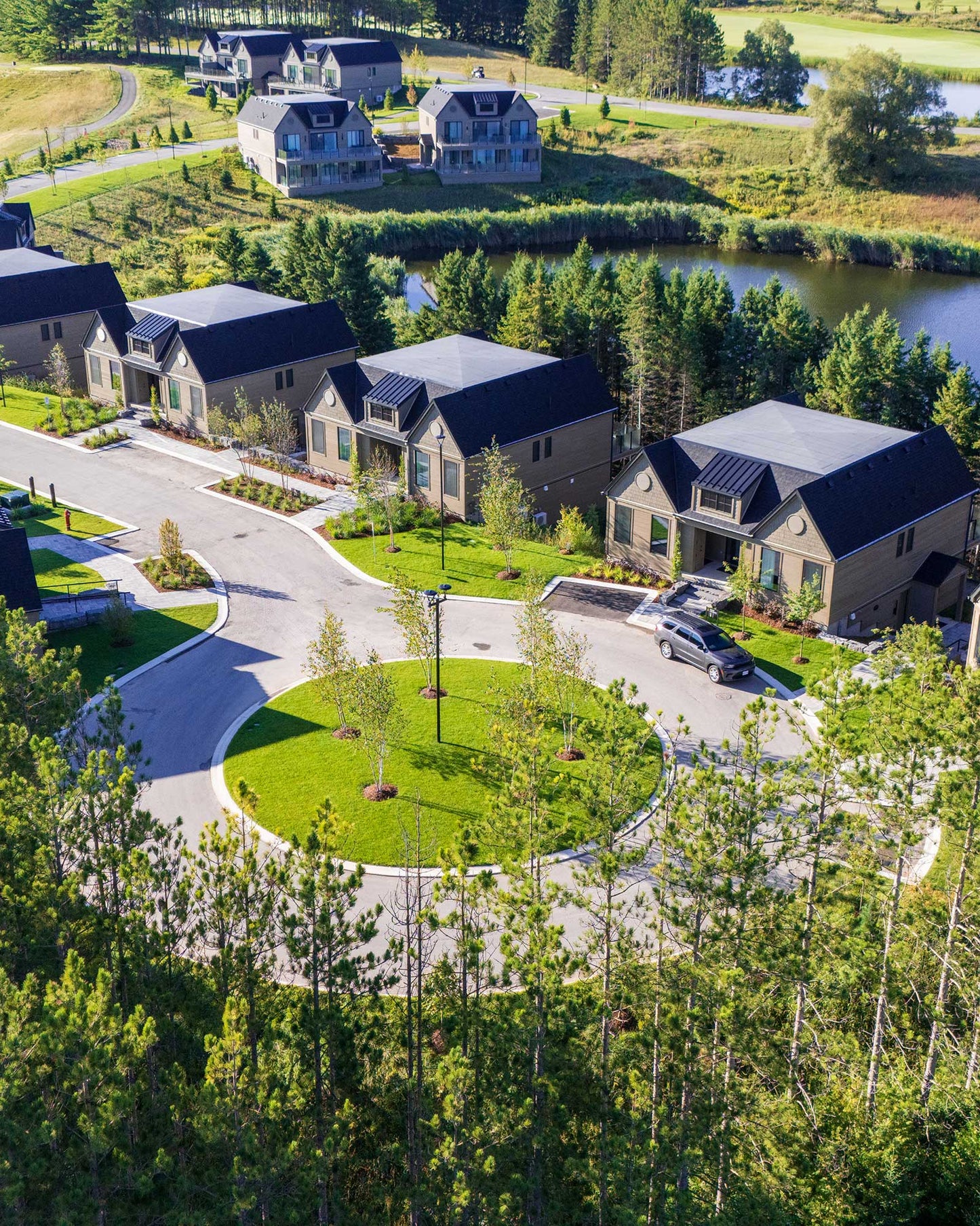 Aerial view of luxury residential golf community with modern houses, manicured lawns, tree-lined streets, and waterfront prop