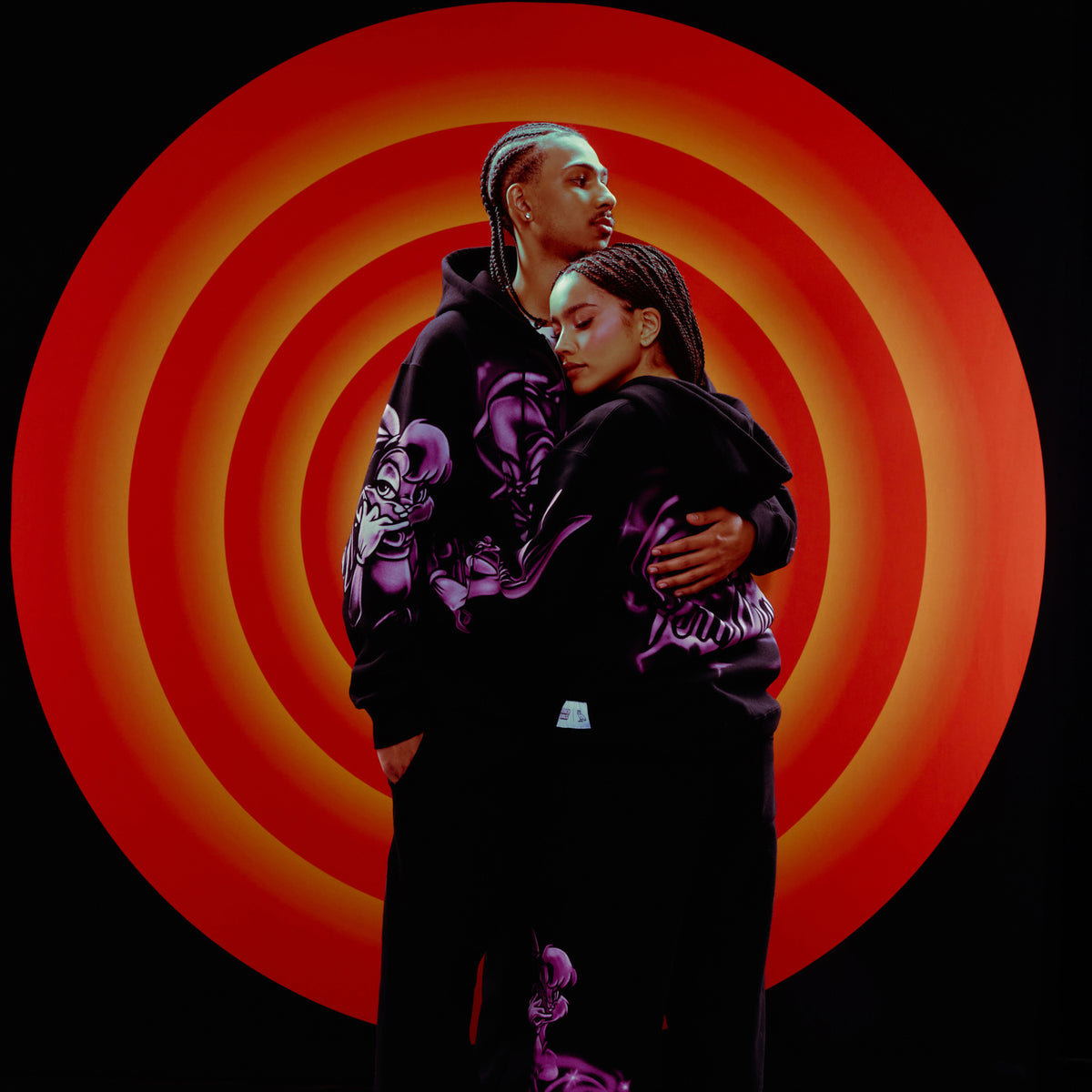 Two people hugging with a vibrant red and orange circular pattern in the background. October's Very Own and Looney Tunes.