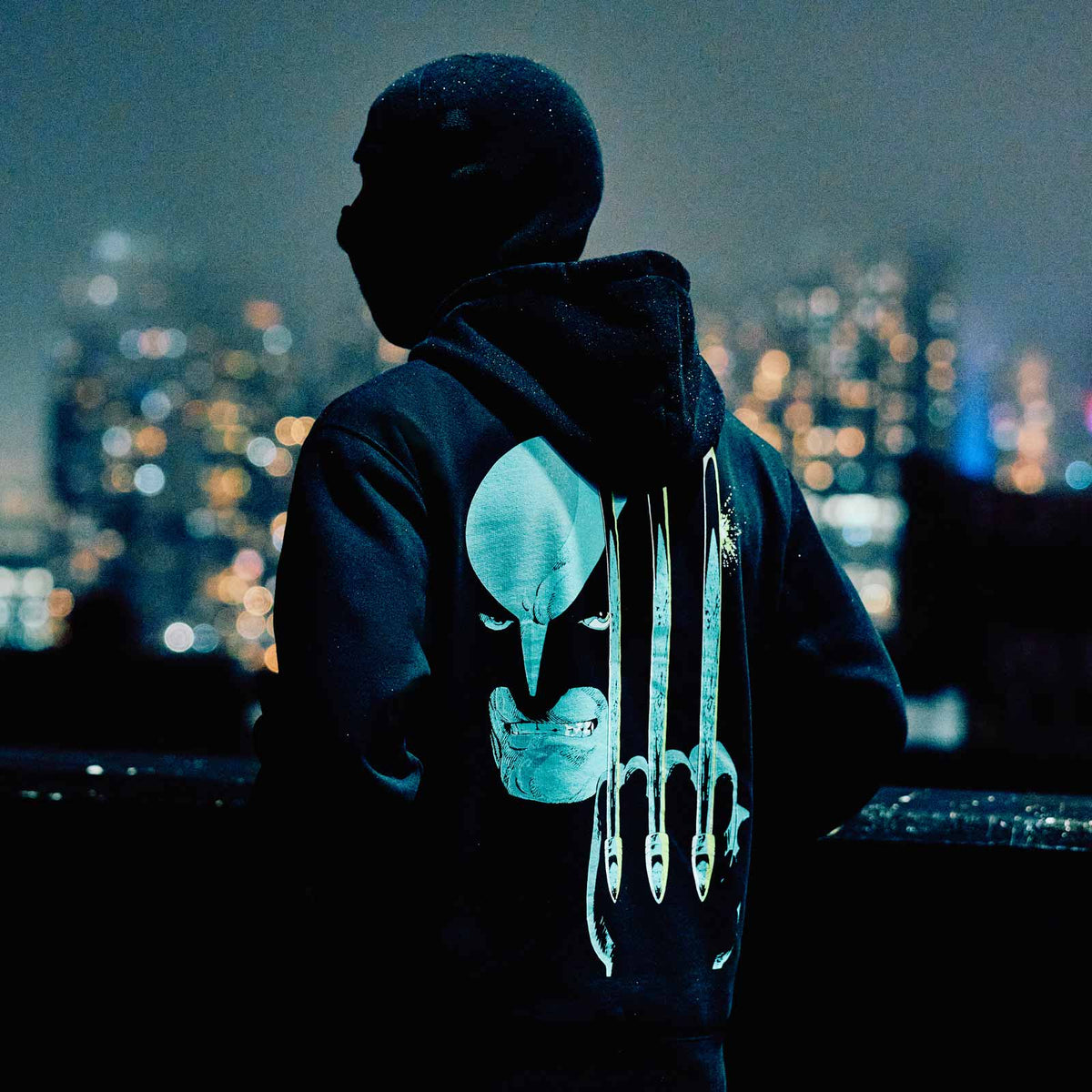 Person wearing a dark hoodie with a glowing design against a cityscape at night. October's Very Own and Marvel.