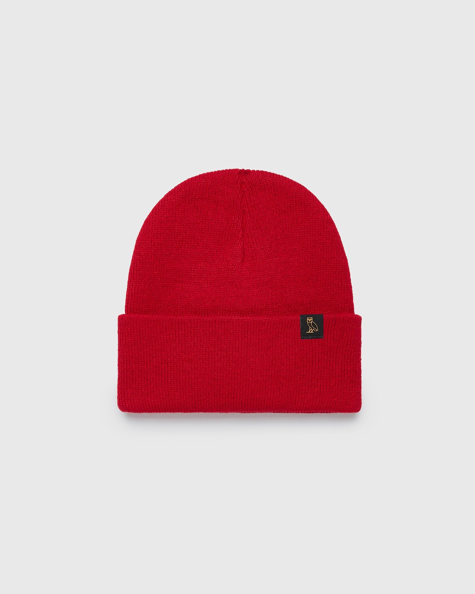 Red knit beanie with ribbed cuff and small dark woven label on front.