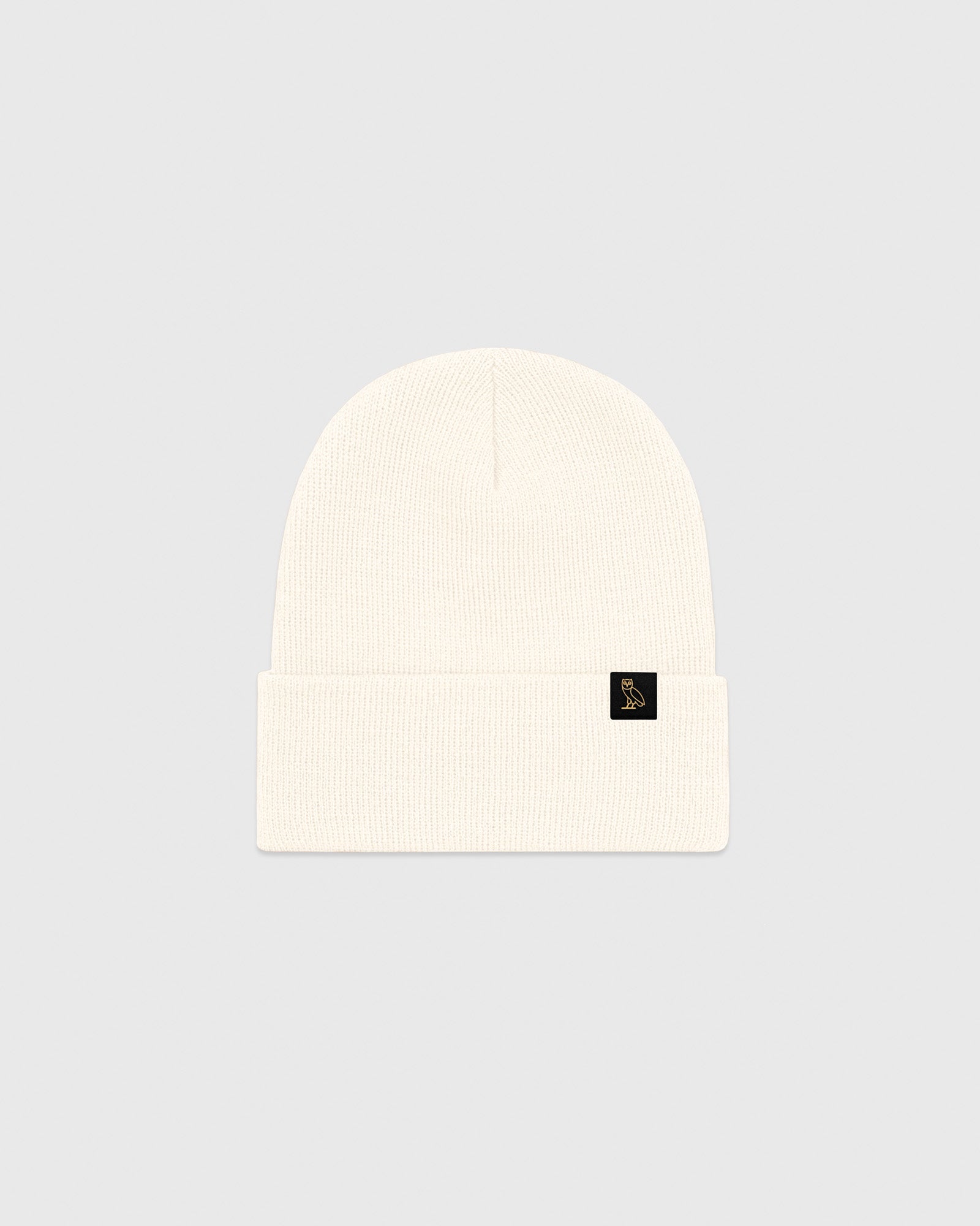 Cream ribbed beanie with small black logo patch on cuff.