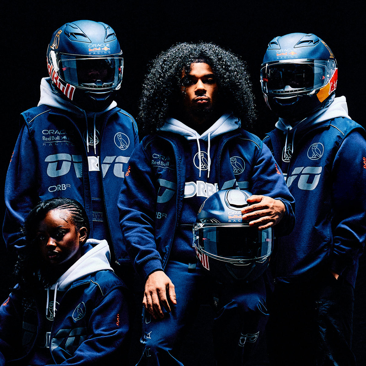 People wearing matching blue October's Very Own x Oracle Red Bull Racing outfits  with 'ORC' branding against a dark background