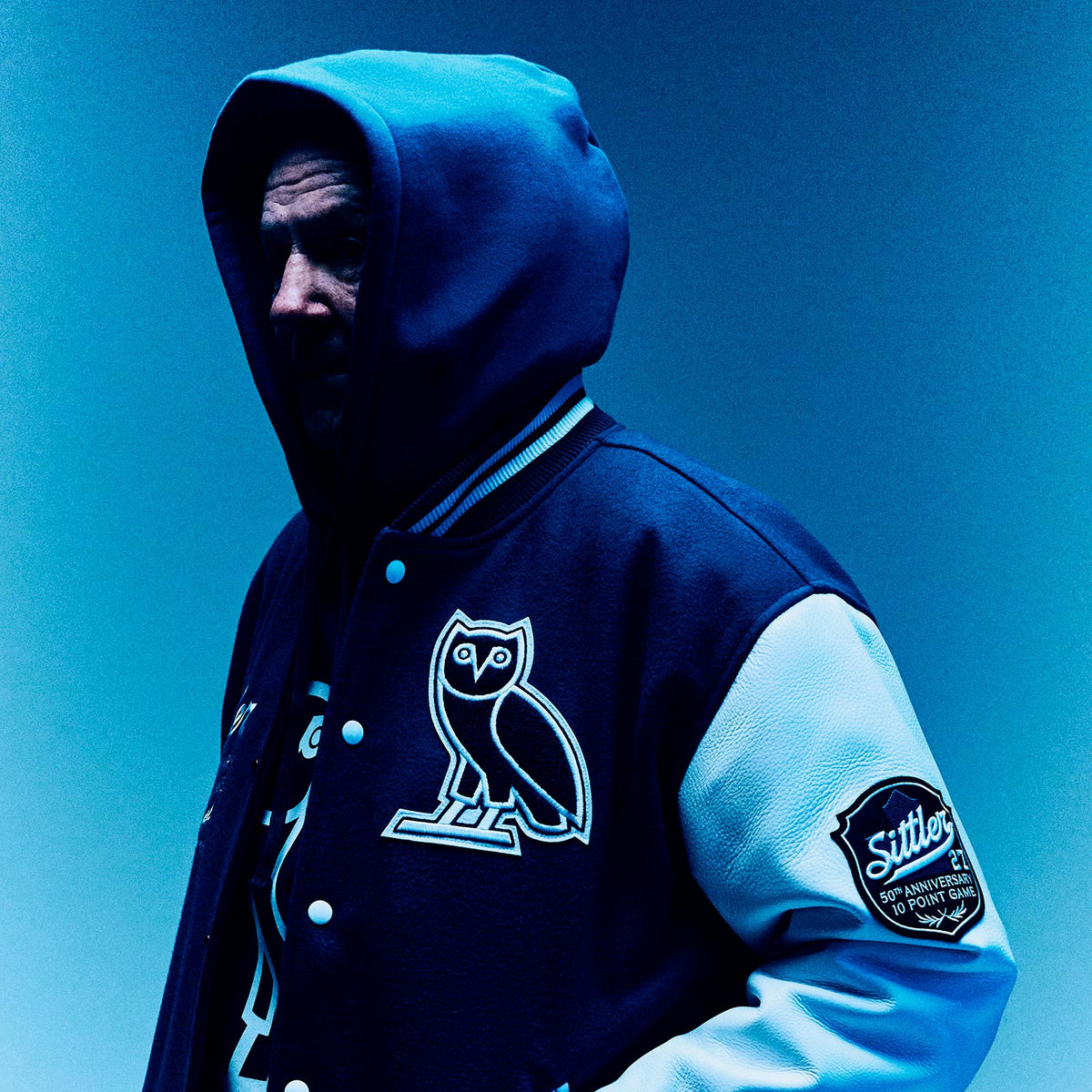 Person wearing a blue hoodie with an October's Very Own owl logo and brand name on a blue background