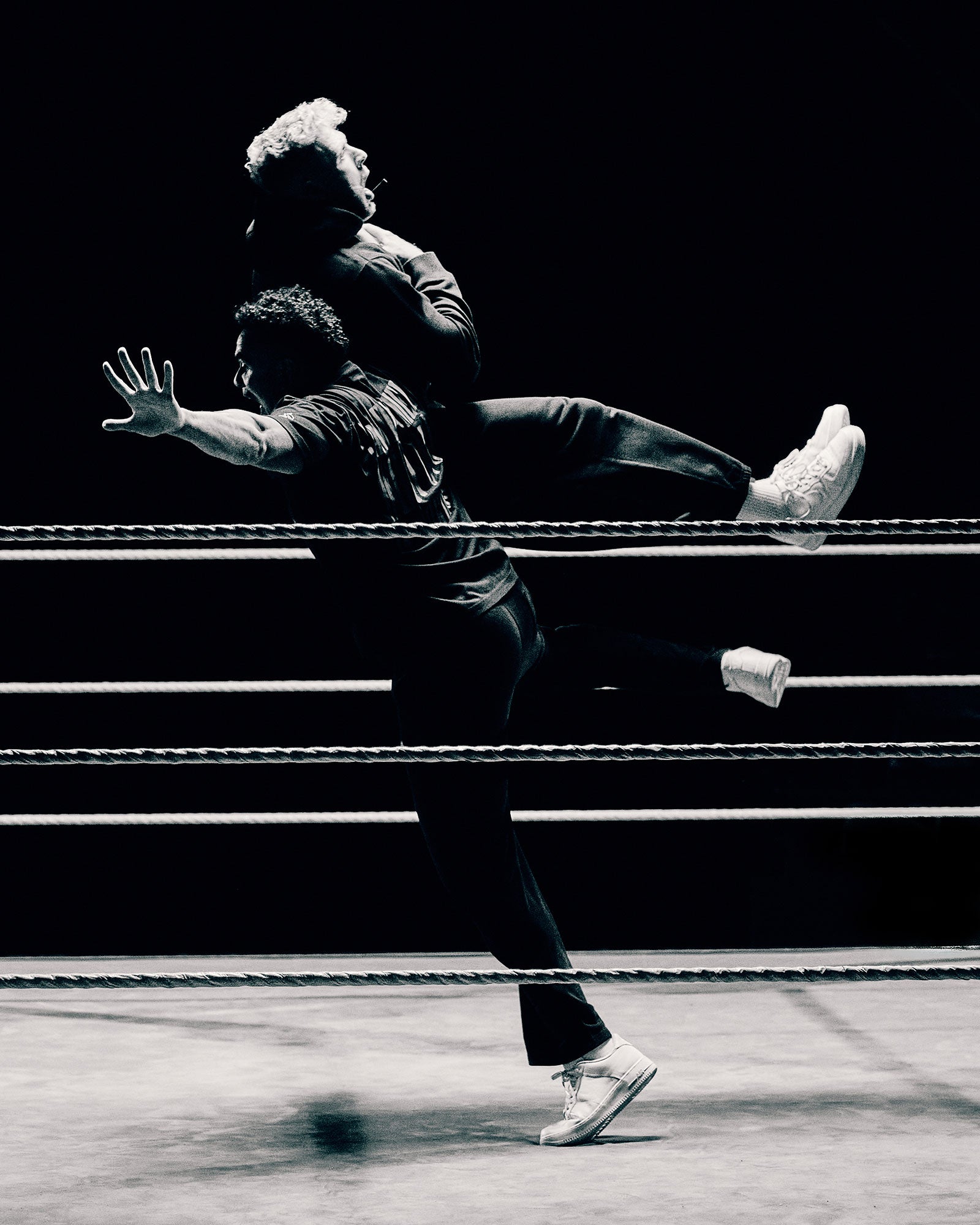 Two wrestlers in a black and white photo, one on top of the other, performing a wrestling move.