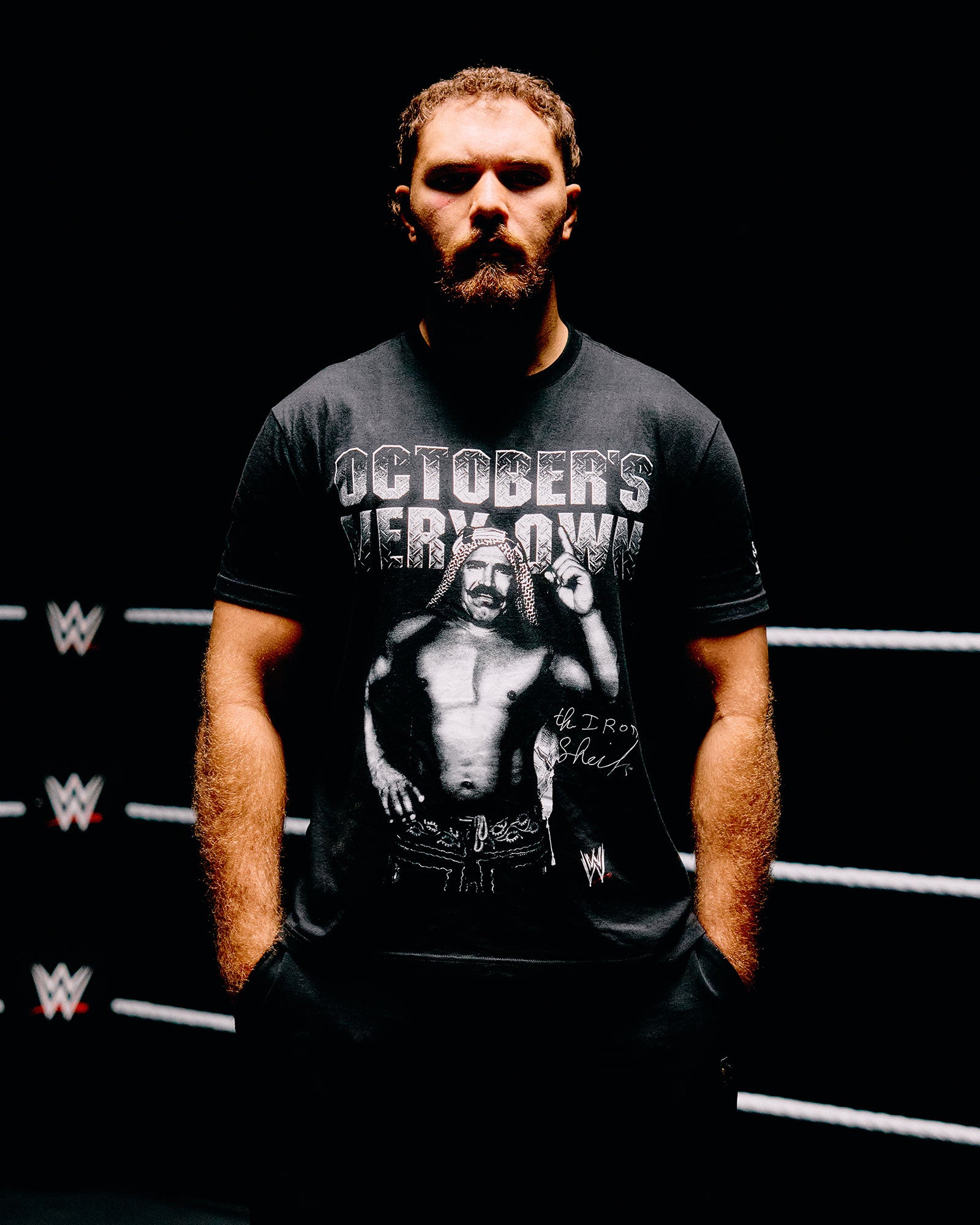 Man wearing a black t-shirt with 'October's Very Own' graphic and text, standing in front of a WWE logo.