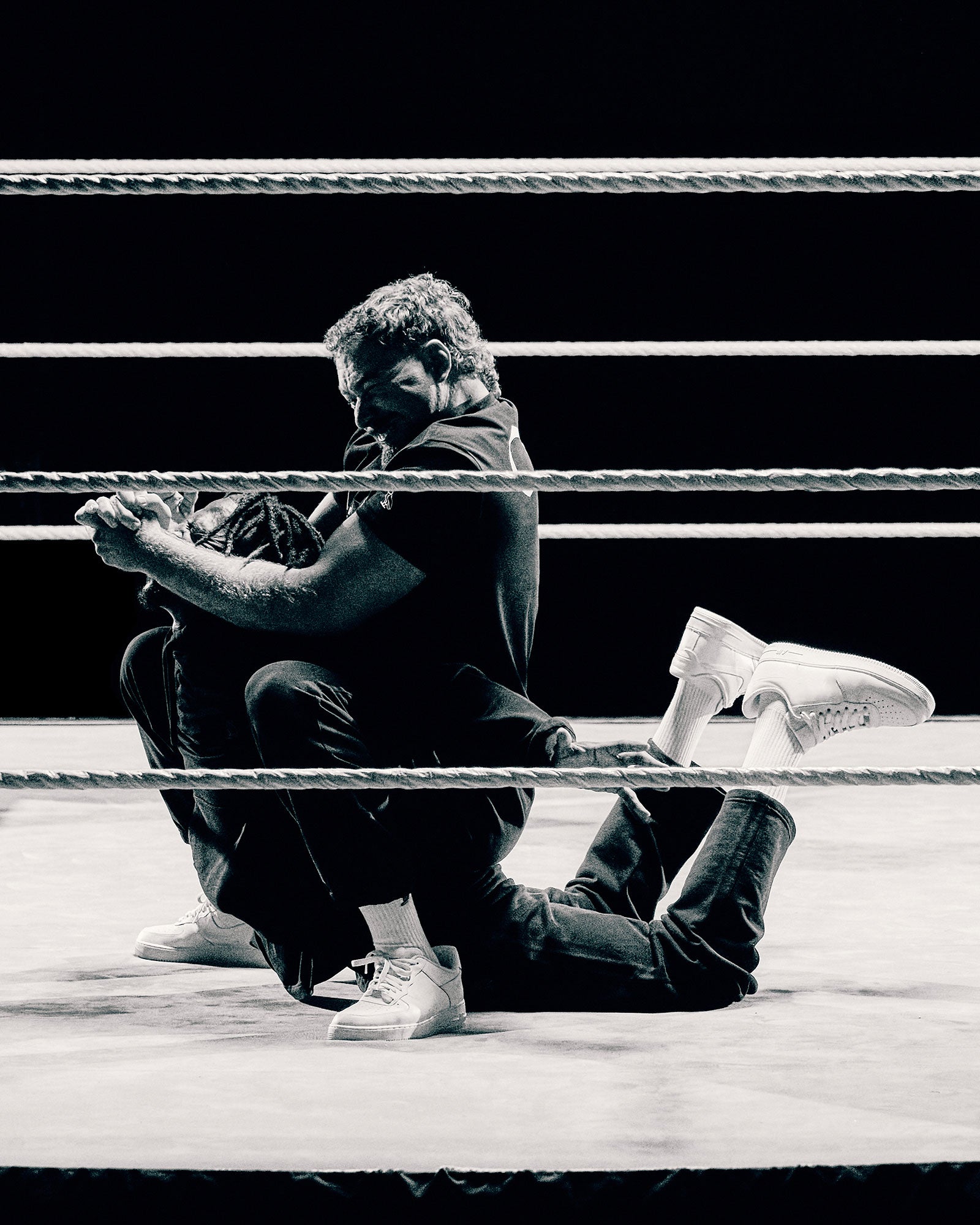 Two individuals in a wrestling ring with one person sitting on top of the other.