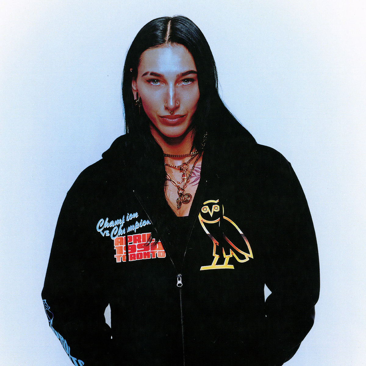 Rhea Ripley wearing a black October's Very Own x WWE hoodie with logos on a white background